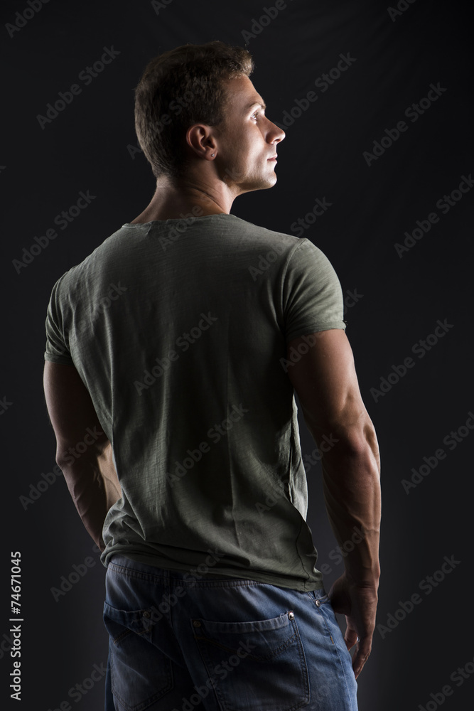 Handsome muscular fit young man's back on dark background Handsome muscular fit young man's back on dark background