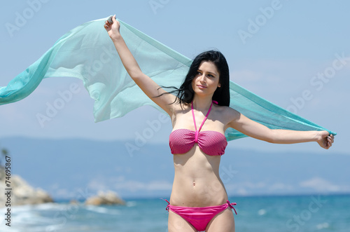 Playful girl in a transparent fabric stands on a sea beach