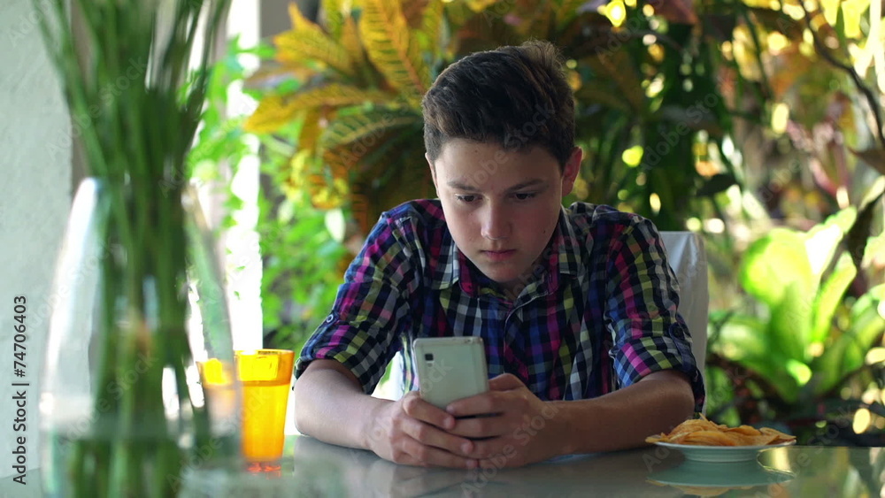 Young teenager sending sms, texting on smartphone by table Young teenager sending sms, texting on smartphone by table