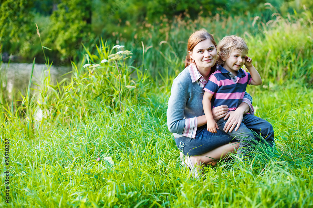 Fototapeta premium Little boy and his mother sitting on grass in summer forest