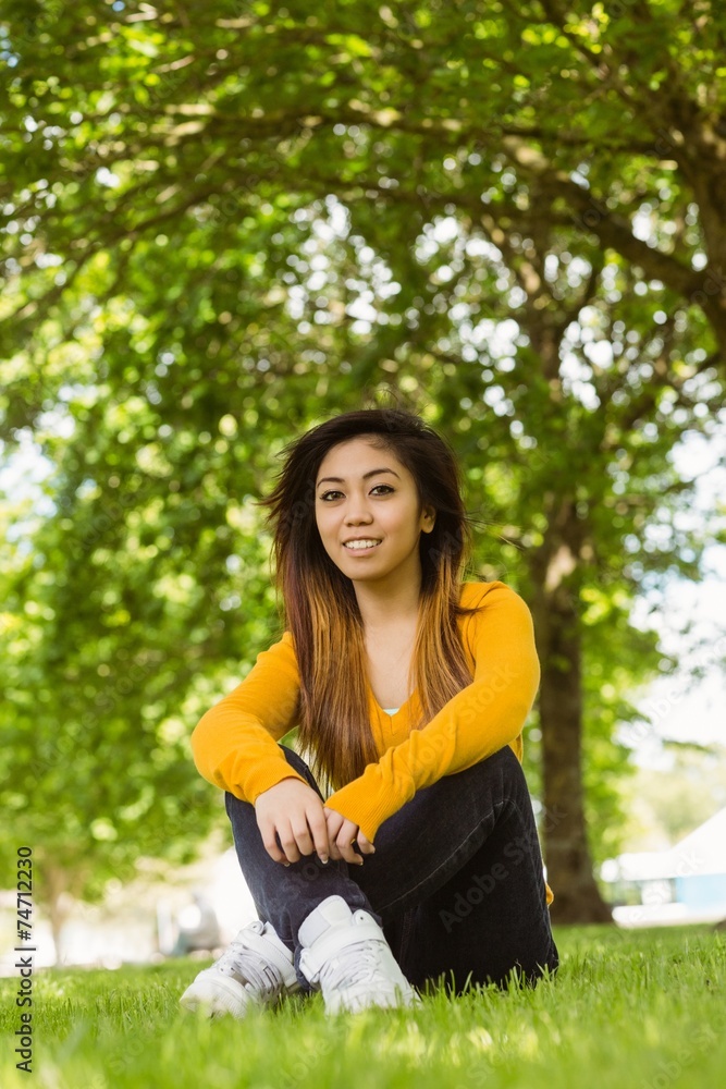 Beautiful relaxed woman sitting on grass at park