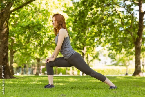 Pretty athletic redhead stretching in park