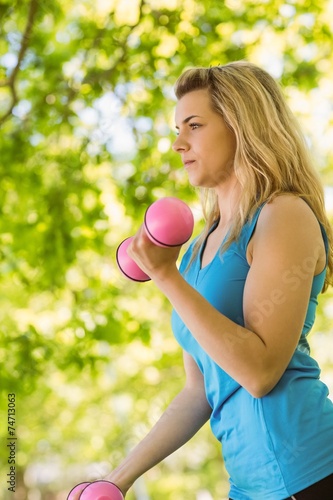 Fit blonde lifting dumbbells in the park