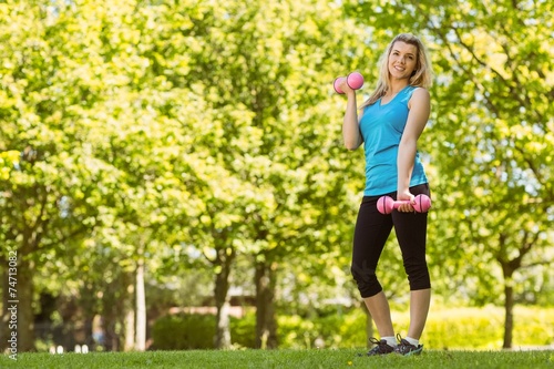 Fit blonde lifting dumbbells in the park