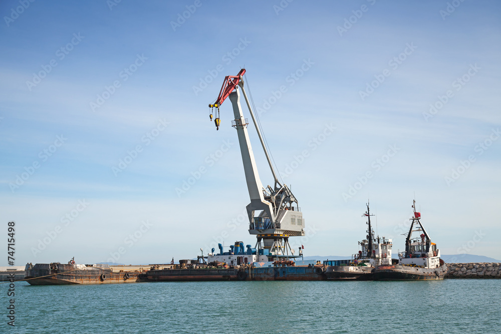 Floating crane and tug boats stand moored in port