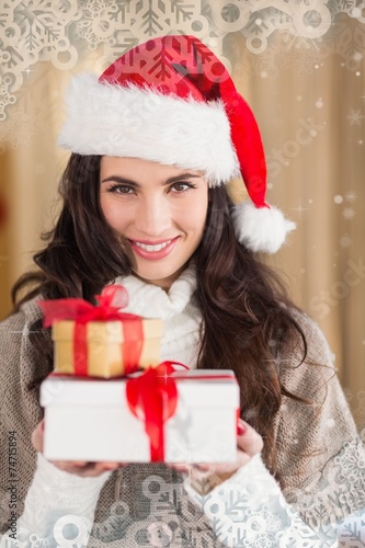 Composite image of festive brunette in santa hat holding gifts