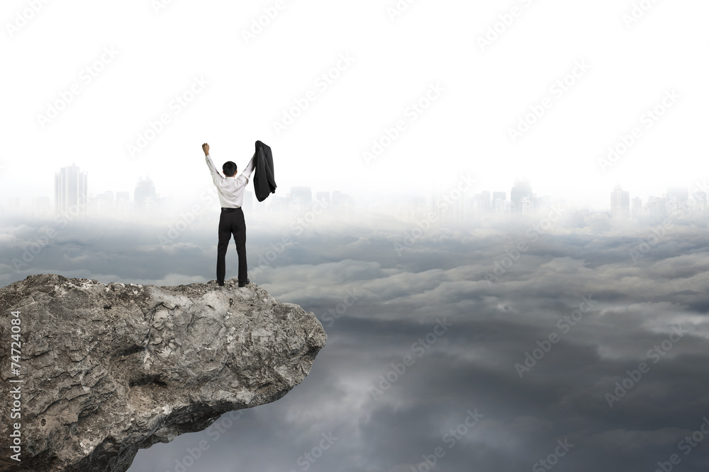 man cheering on cliff with gray cloudy sky cityscape background