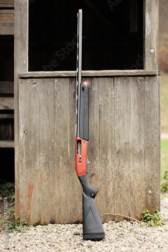 Modern shotgun leaning against a wood cabin
