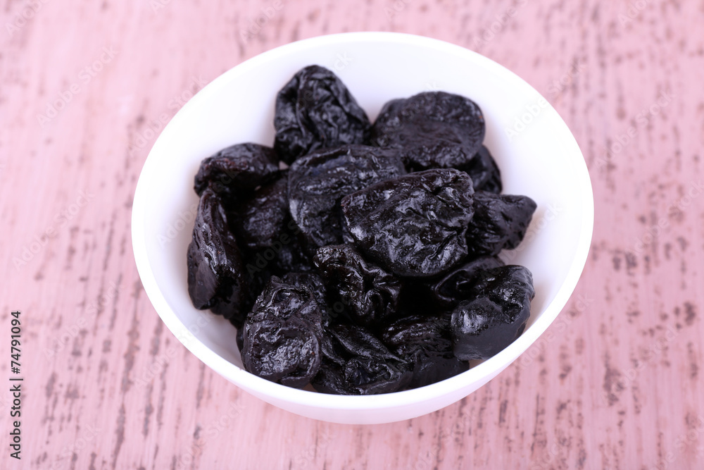 Bowl with heap of prunes on color wooden background Bowl with heap of prunes on color wooden background