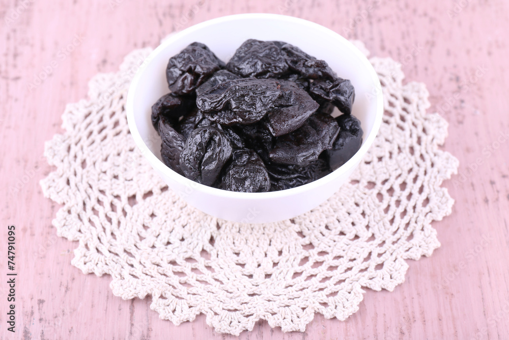 Prunes in bowl on lace doily on color wooden background Prunes in bowl on lace doily on color wooden background