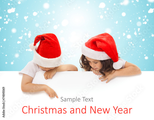 Happy little kids in Santa hat peeking from behind blank sign