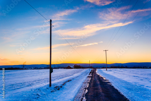 Sunset over a country road through snow covered fields in rural photo
