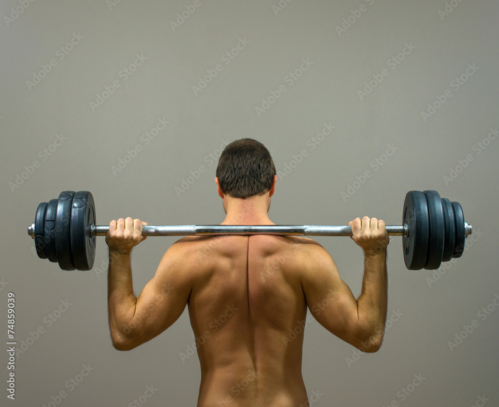 Muscular man doing exercises with barbell. Back view.