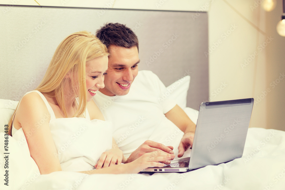 smiling couple in bed with laptop computer