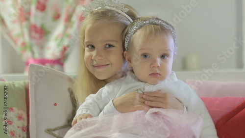 Little cute girl sitting on couch and hugging her little sister