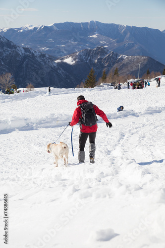 man walks the dog on snowy winter day in mountain