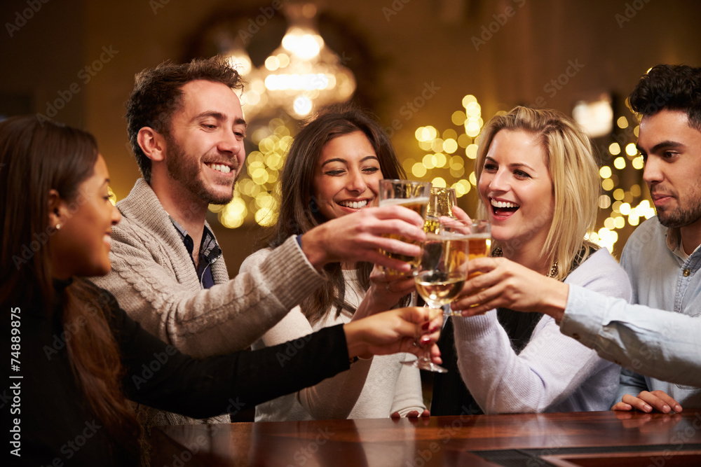 Group Of Friends Enjoying Evening Drinks In Bar - obrazy, fototapety, plakaty 