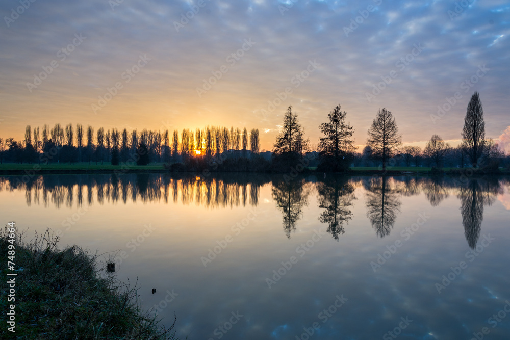 Fototapeta premium Winter sunset in the shore of a lake with clouds reflected in th