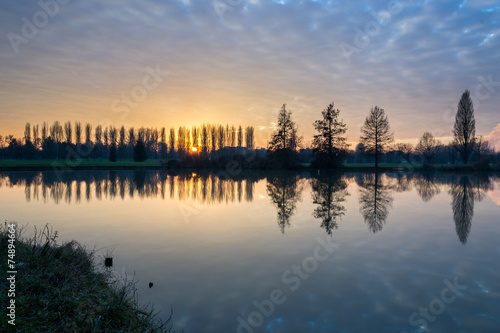 Winter sunset in the shore of a lake with clouds reflected in th