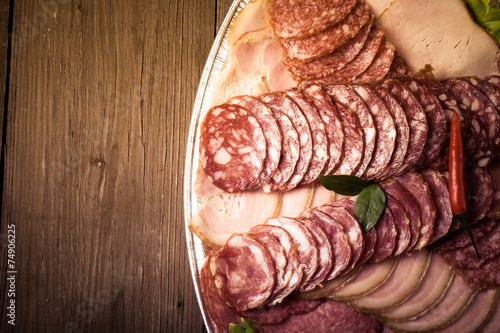 plate with different sliced sausage on an old wooden table. With