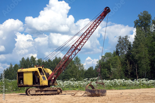 Excavator standing on sand near forest on summer day