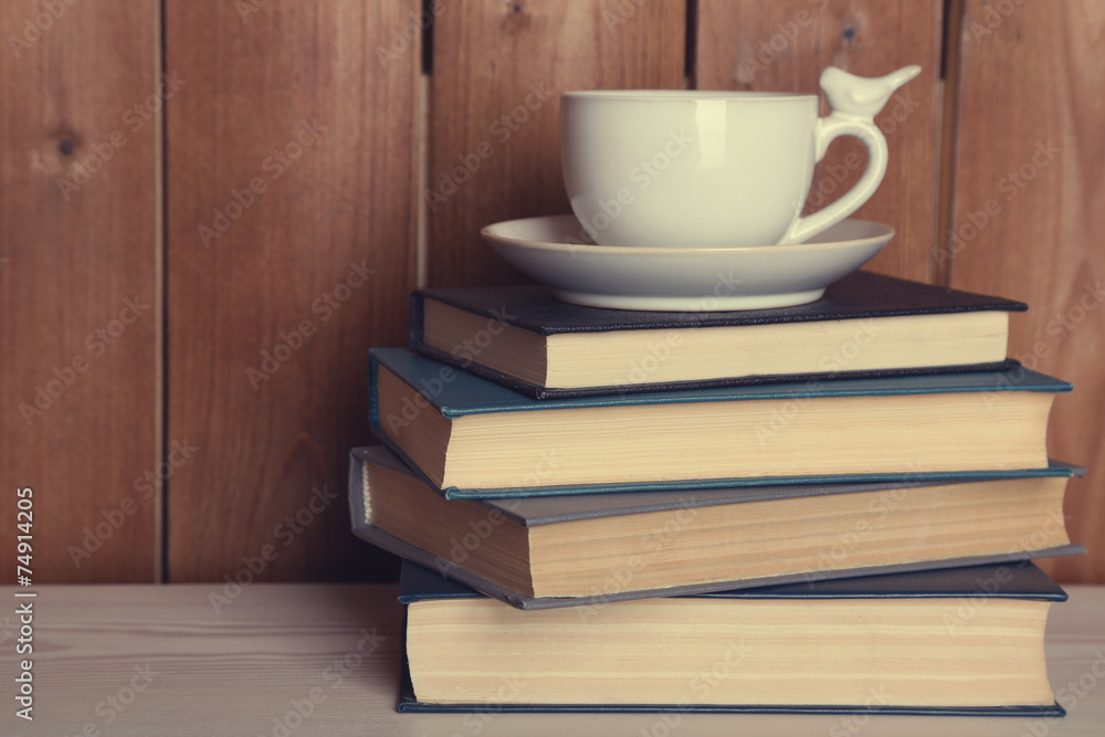 Pile of books with cup on tabletop and wooden background Pile of books with cup on tabletop and wooden background