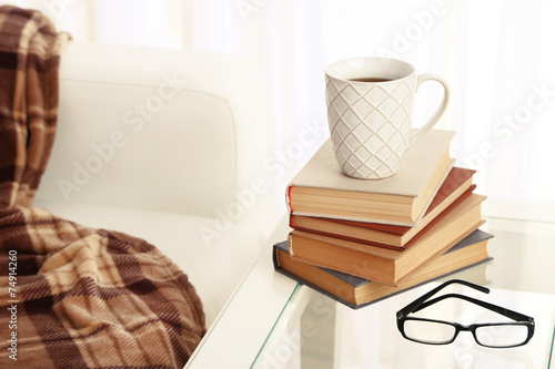 Tabletop with pile of books, cup and glasses near the sofa