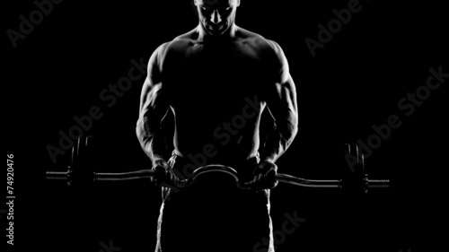 Close up of young muscular man lifting weights over dark backgro