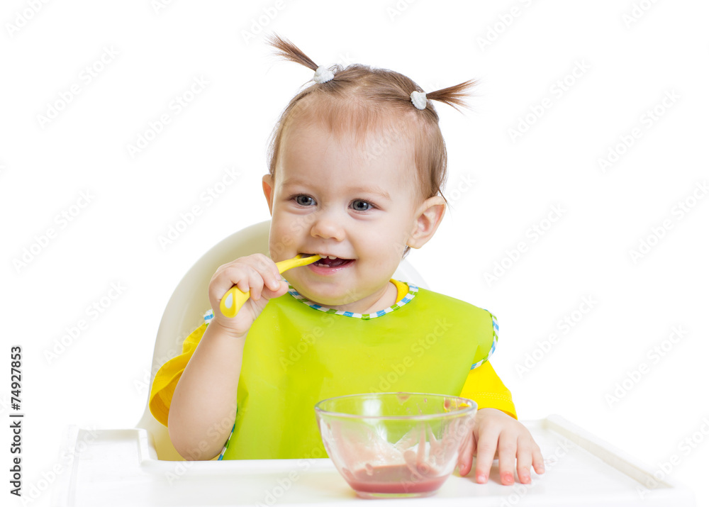 Baby eating with spoon sitting at table Baby eating with spoon sitting at table