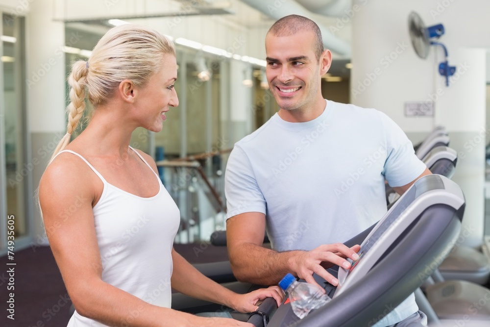 Trainer assisting woman with treadmill screen options at gym Trainer assisting woman with treadmill screen options at gym