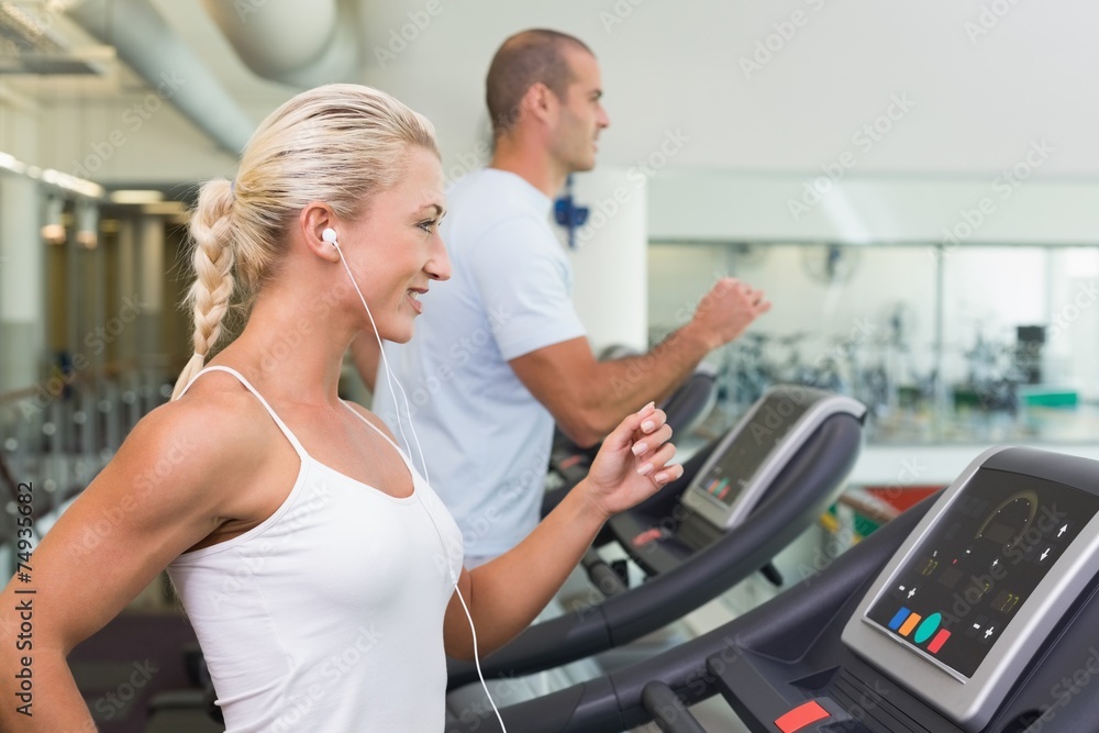 Side view of couple running on treadmills at gym Side view of couple running on treadmills at gym
