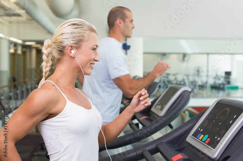 Side view of couple running on treadmills at gym