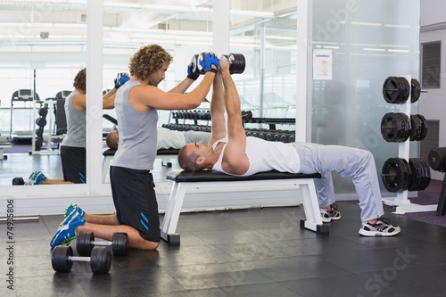 Male trainer assisting young man with dumbbells in gym