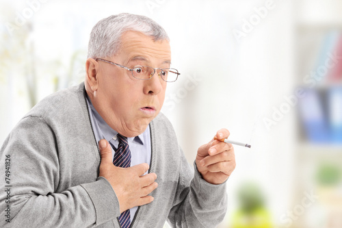 Senior man choking from the smoke of a cigarette