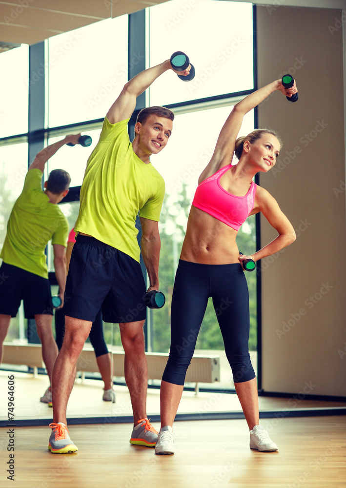 Naklejka premium smiling man and woman with dumbbells in gym