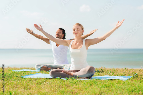 smiling couple making yoga exercises outdoors