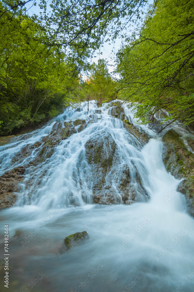 Beautiful waterfall in the forest between green trees Beautiful waterfall in the forest between green trees