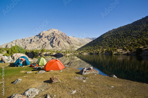 blue mountain lake reflects high rocks with camp near it