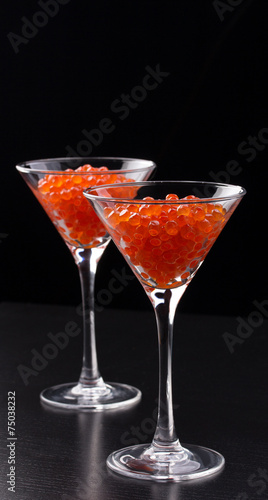 Red caviar in wineglasses on black background