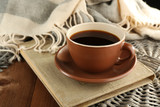 Cup of coffee on book near plaid on wooden table background