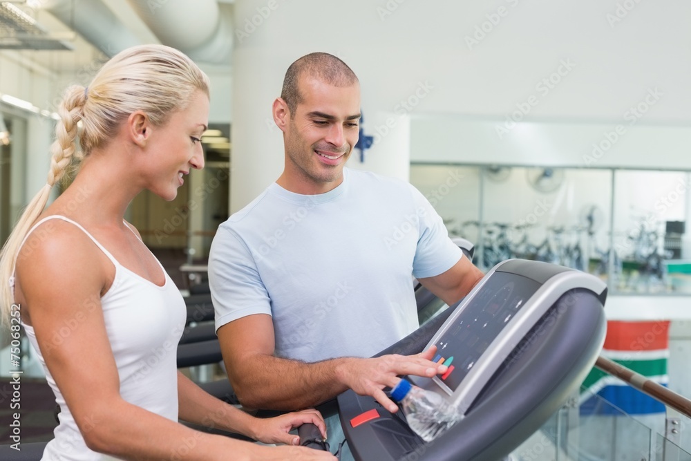 Trainer assisting woman with treadmill screen options at gym Trainer assisting woman with treadmill screen options at gym