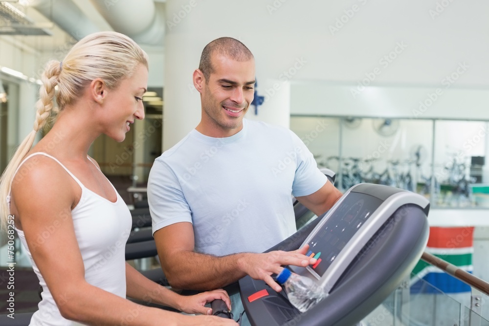 Trainer assisting woman with treadmill screen options at gym