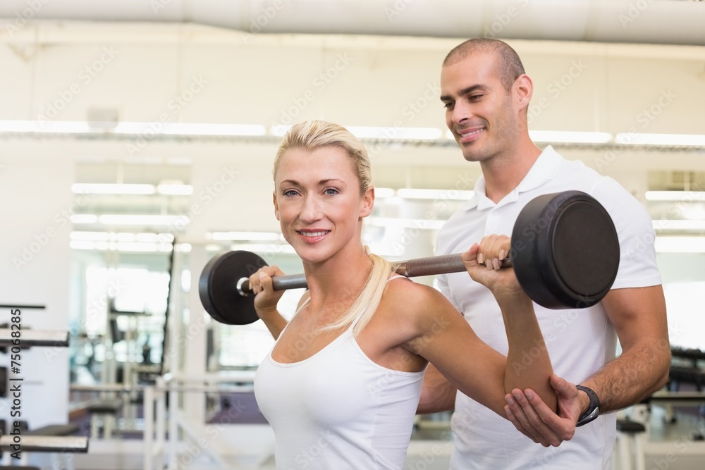 Trainer helping woman with lifting barbell in gym Trainer helping woman with lifting barbell in gym