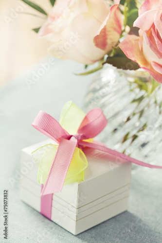 Gift box decorated with bow and roses in vase