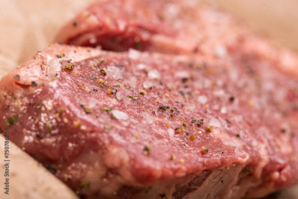 Raw beef steak seasoned with salt and pepper on a dark paper Raw beef steak seasoned with salt and pepper on a dark paper