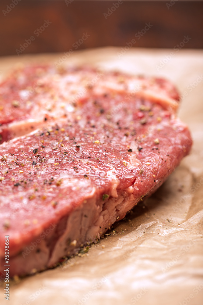 Raw beef steak seasoned with salt and pepper on a dark paper Raw beef steak seasoned with salt and pepper on a dark paper