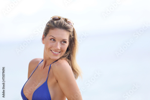 Blond woman in bikini with eyeglasses posing by the beach