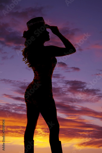 cowgirl standing in the sunset silhouette holding hat