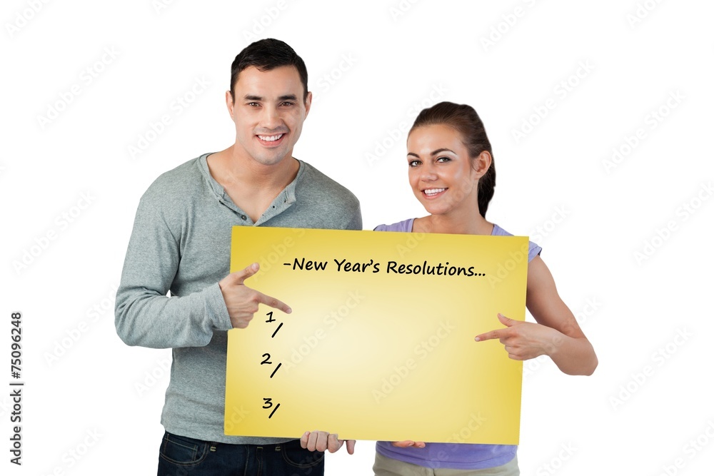 Smiling young couple pointing at sign they are holding Smiling young couple pointing at sign they are holding