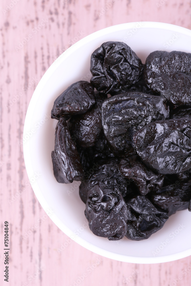 Bowl with heap of prunes on color wooden background Bowl with heap of prunes on color wooden background